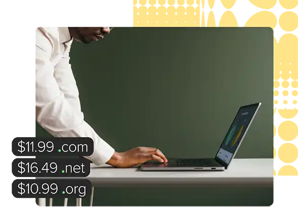 A man stands over a desk with both hands on the keyboard of a laptop.