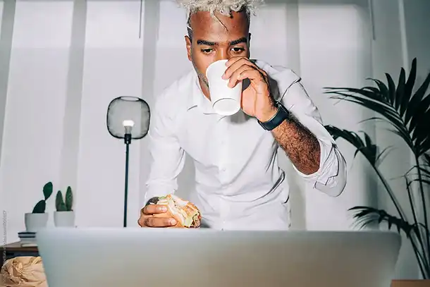 man having lunch while looking at laptop